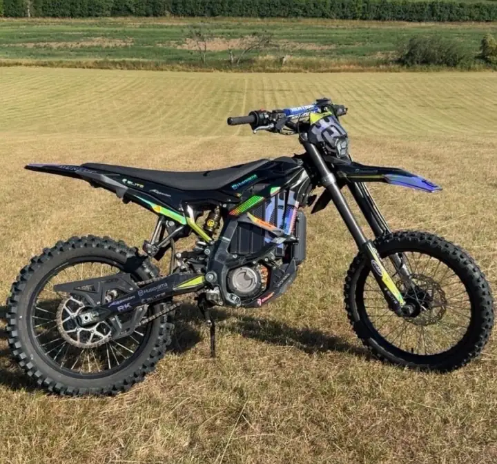 Black electric dirt bike with Husqvarna-style graphics parked side-on in a mown field