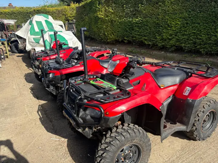 A row of red Honda TRX farm quads with snorkels, lined up on a farmyard track