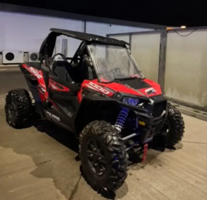 Red and black Polaris RZR 1000 with a roof, windscreen and blue shock springs, parked on concrete at night