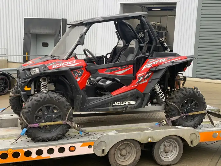 Red Polaris RZR XP 1000 strapped down on a car transporter trailer